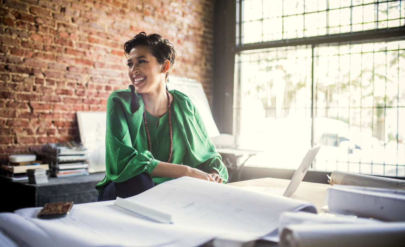 A business owner smiles while looking over paper plans spread across her desk