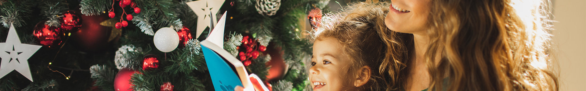 Mum reading a book with her daughter sat infront of a Christmas tree